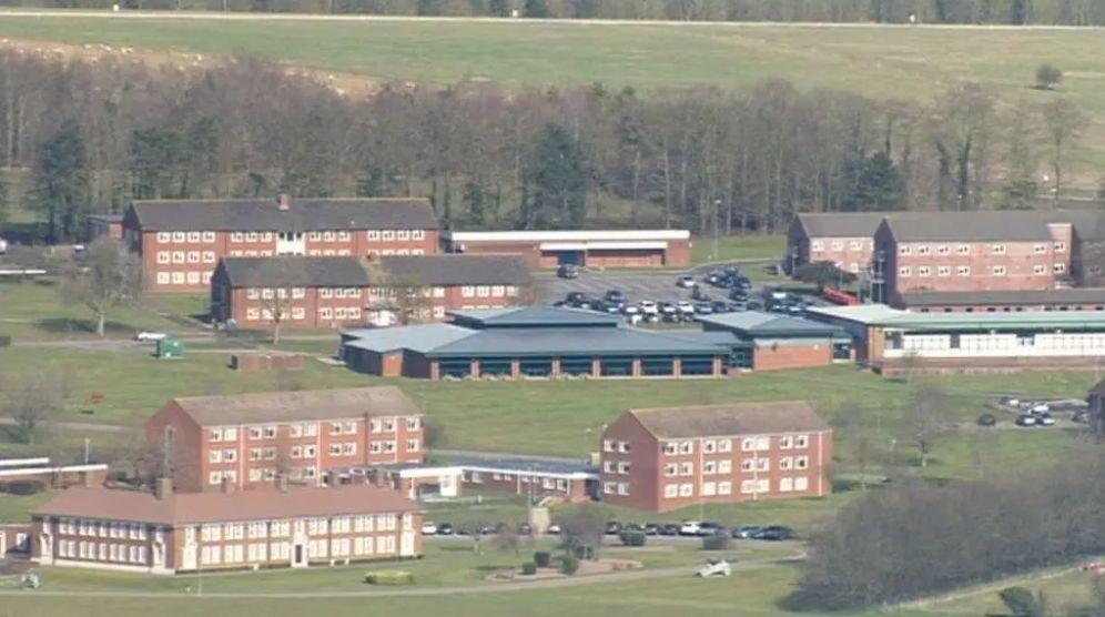 An aerial image of Larkhill Camp. It shows about half a dozen brown, brick buildings ranging between two and four storeys high. They are among grassy areas with trees in the background. 