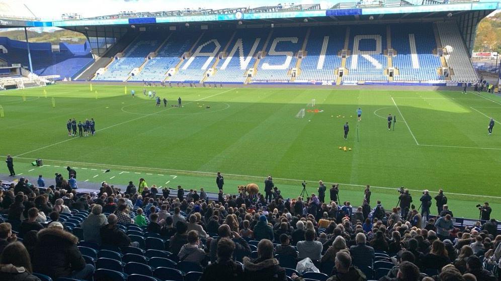 A crowd of fans photographed from behind, they are seated in a stand watching training at Sheffield Wednesday