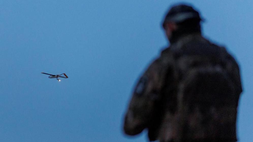 A Ukrainian soldier operating a drone, which is flying in the air in the background