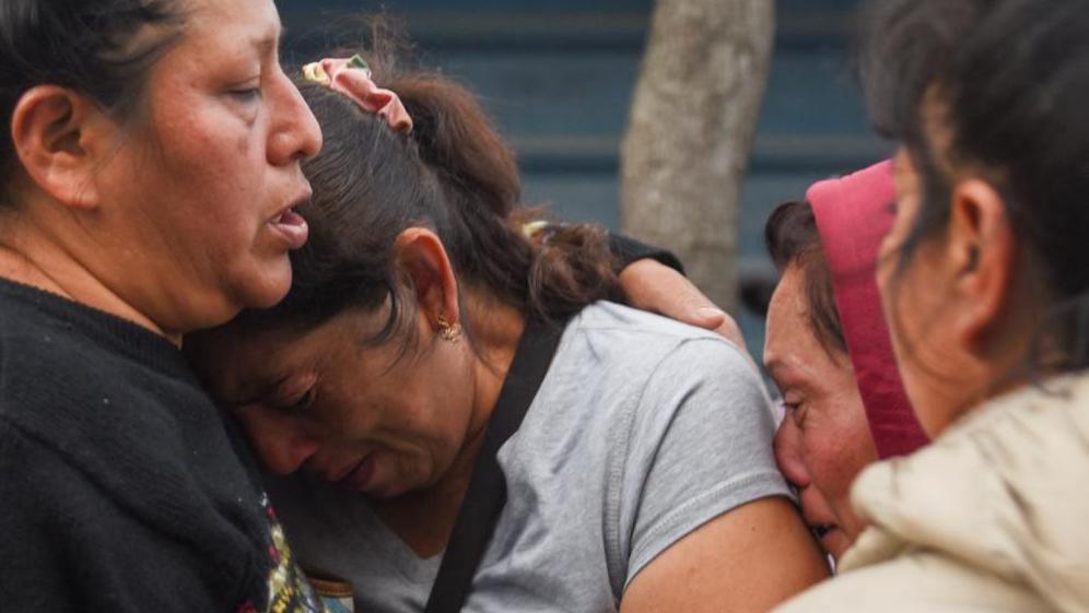 A woman consoles another woman at the scene of the crash. Two other women stand by, one of them can be seen crying. 