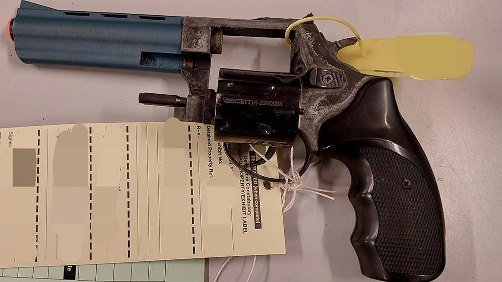 A revolver-style pistol with a blue barrel and tags tied to its trigger guard and hammer