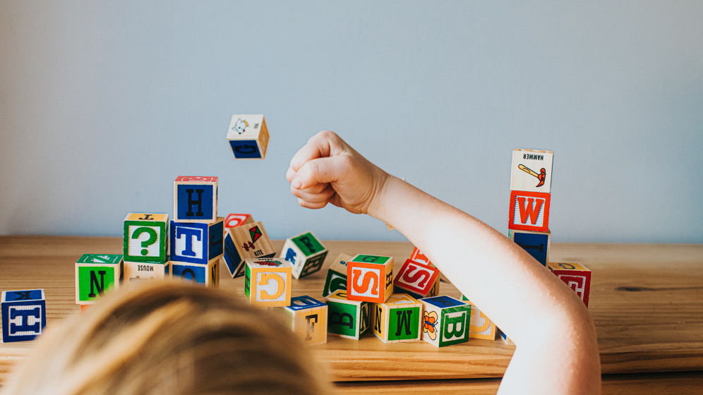 A child smashes a tower of blocks with their fist. Only the back of the child's head and their fist is in view.