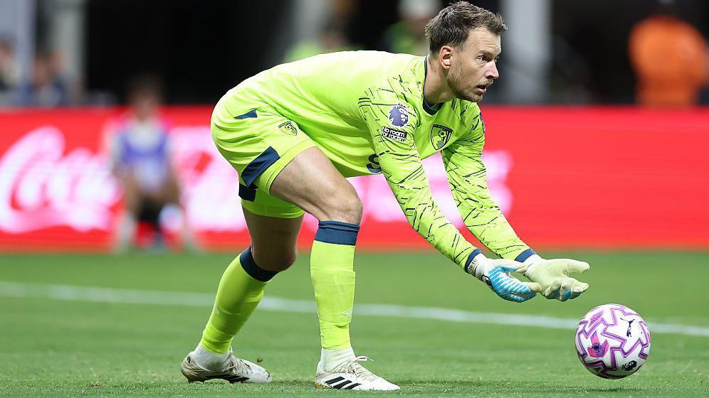 A goalkeeper wearing a green jersey rolls a football.