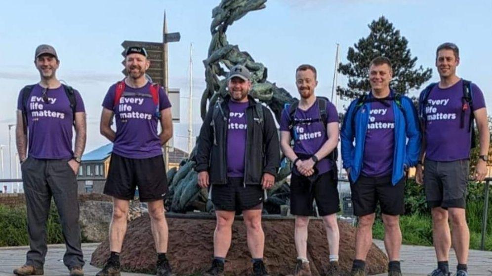 Six men stand in a row and are all wearing purple t-shirts which say 'Every Life Matters'