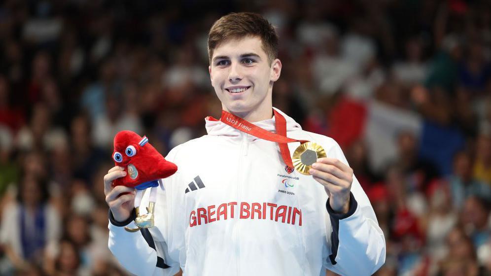 William Ellard holds his Paralympic gold medal on the podium.