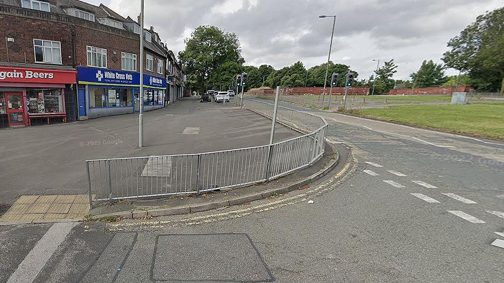 Muirhead Avenue in West Derby showing a row of shops and trees lining the road and traffic lights