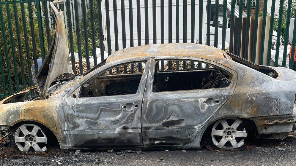 A burnt car abandoned in front of a gate