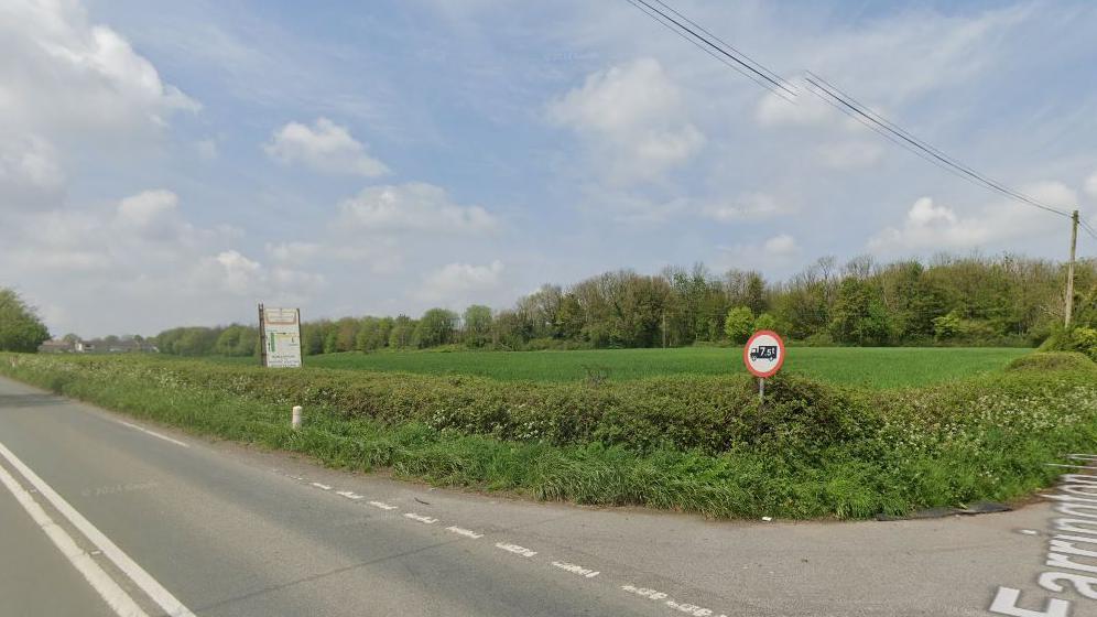 General view of junction with green bushes running along and blue sky.