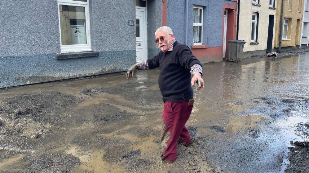 Man walks through wet mud on a flood-hit street in Cwmtillery. south Wales