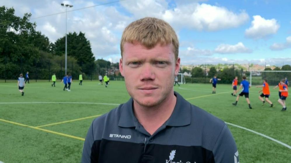 Dan Jackson wearing a grey and black T-shirt standing on a football pitch.