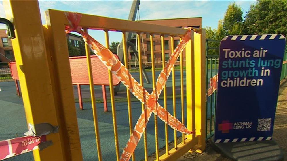 Tape saying 'toxic air' is wrapped around a gate at a Birmingham park near a sign that says 'Toxic air stunts lung growth in children'