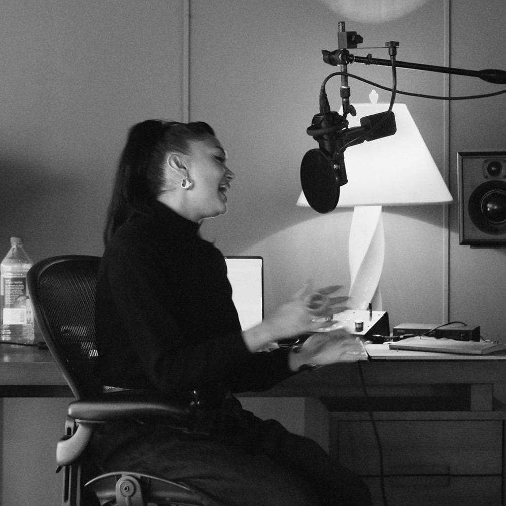 A black and white photograph shows Joy Crookes recording vocals for her album, while sitting down