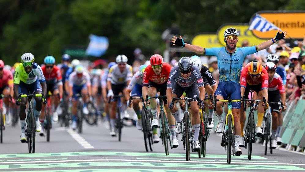 mark cavendish crossing the finish line surrounded by other cyclists