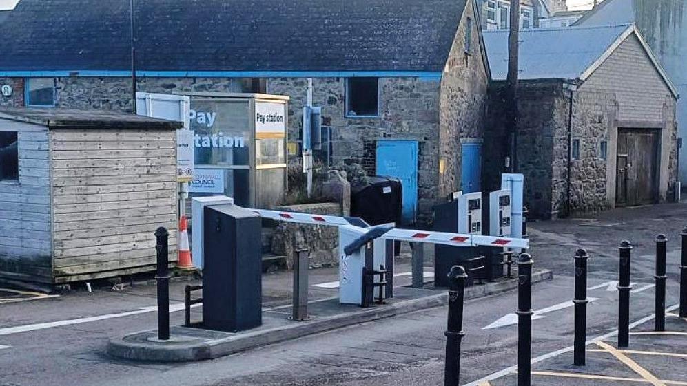 A barrier is in place besides a car park and there is a pay station to the left of it.