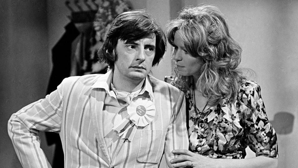 A man and a woman stand in conversation.