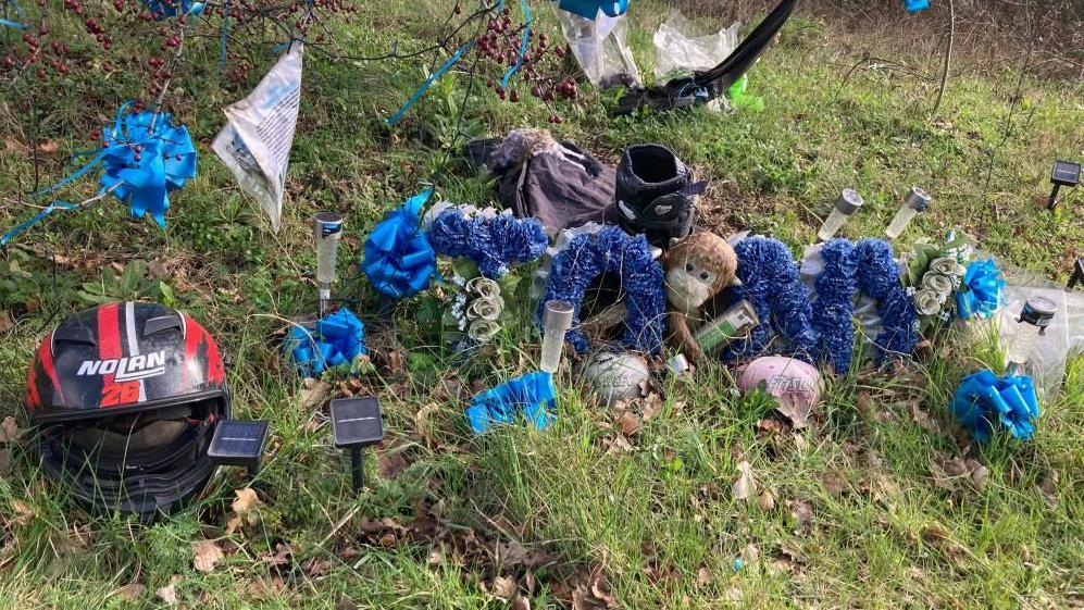 The tribute to the deceased traffic accident victim - a motorcycle helmet, cuddly toys, blue ribbons on the branch, and letters from his family