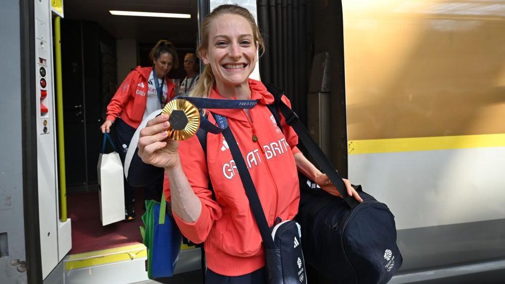  Bryony Page  holding up her gold medal while getting off the Eurostar