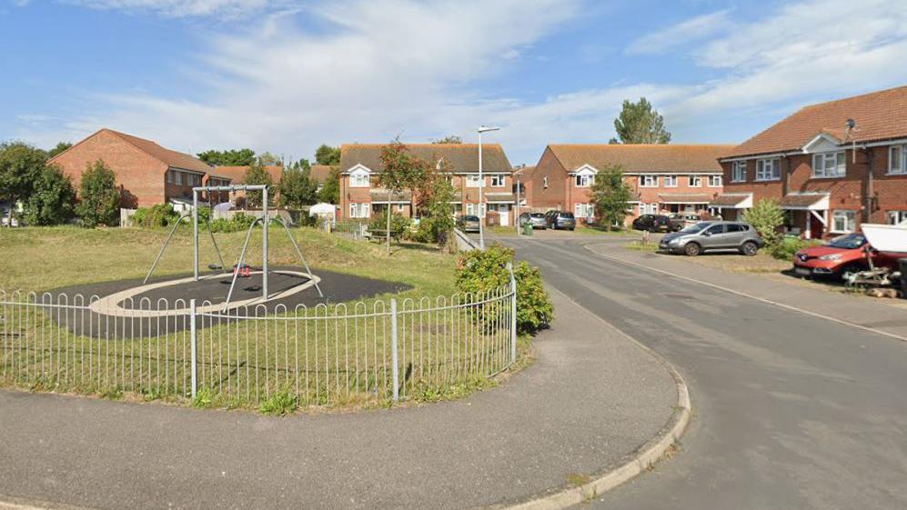 A close of red brick house with a children's playground to the left.