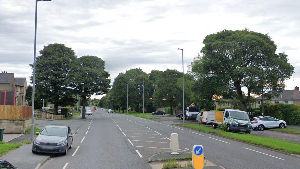 View down Halifax Road in Bradford with trees on either side and a number of cars parked on verges