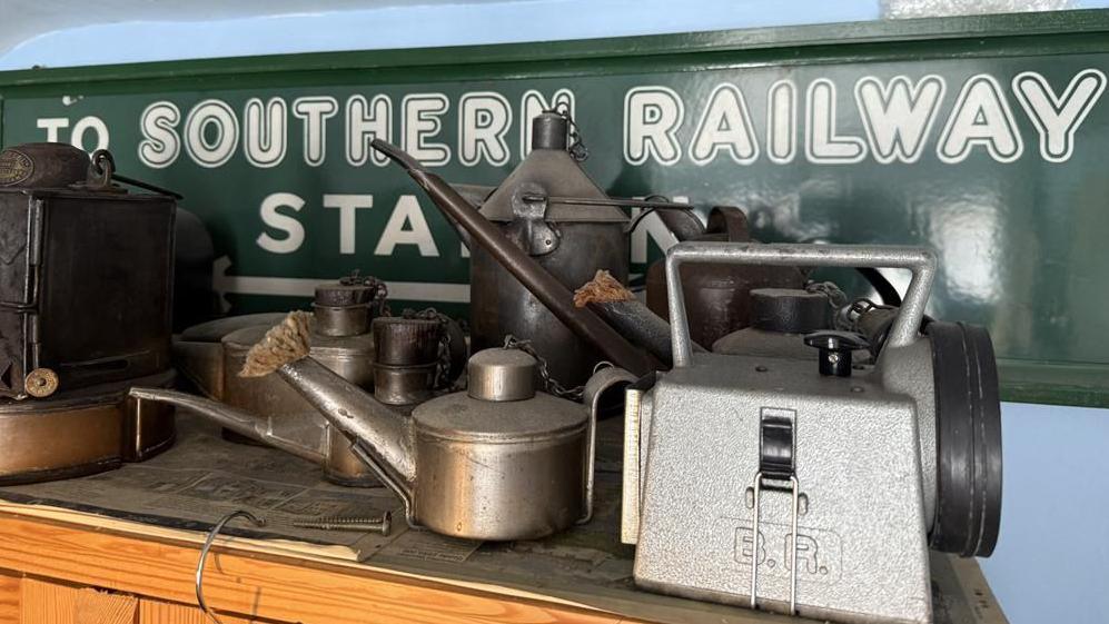A vintage green 'Southern Railway' sign with old lamps and technical items sitting on a table in front