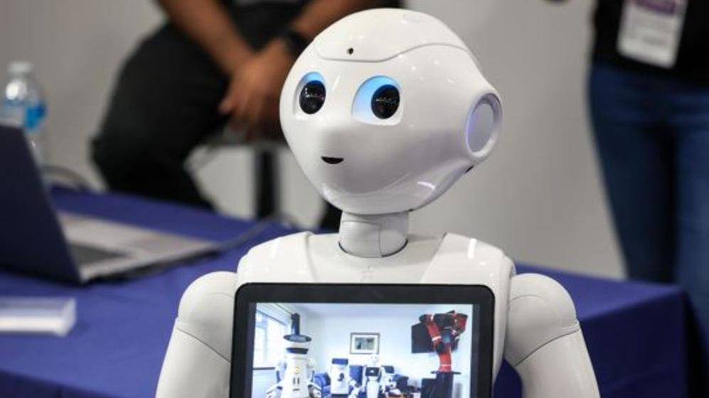 A white robot, with the image showing its head and the top part of its body. A screen is on its chest.  