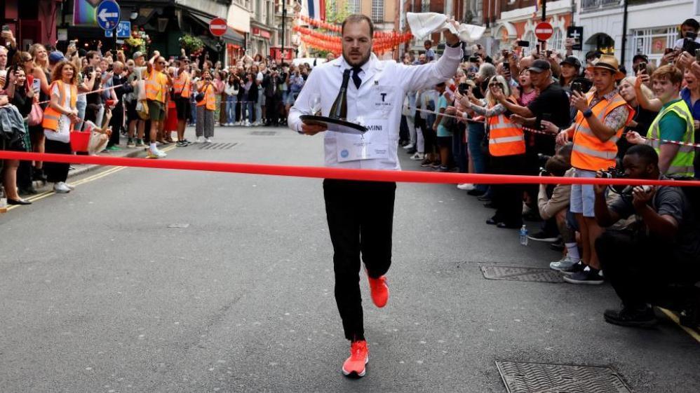 Alessandro Belometti from Bar Termini crosses the finish line to win the annual waiters' race during the 50th anniversary of the Soho Village Fete in London, Britain, July 20, 2025