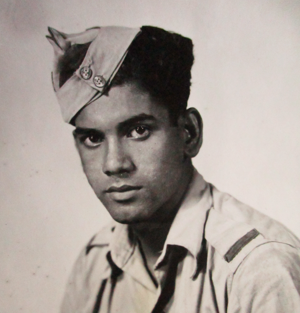 A man wearing a forage cap and an open-neck shirt looks towards the camera.