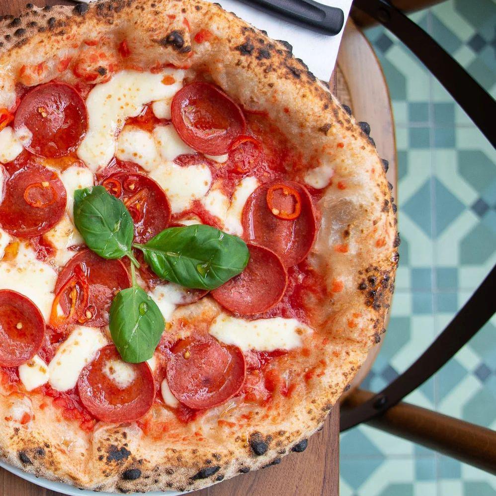 The pizza is topped with cheese, tomato sauce, pepperoni and basil. It is on a plate on a table next to a napkin with a knife and fork.