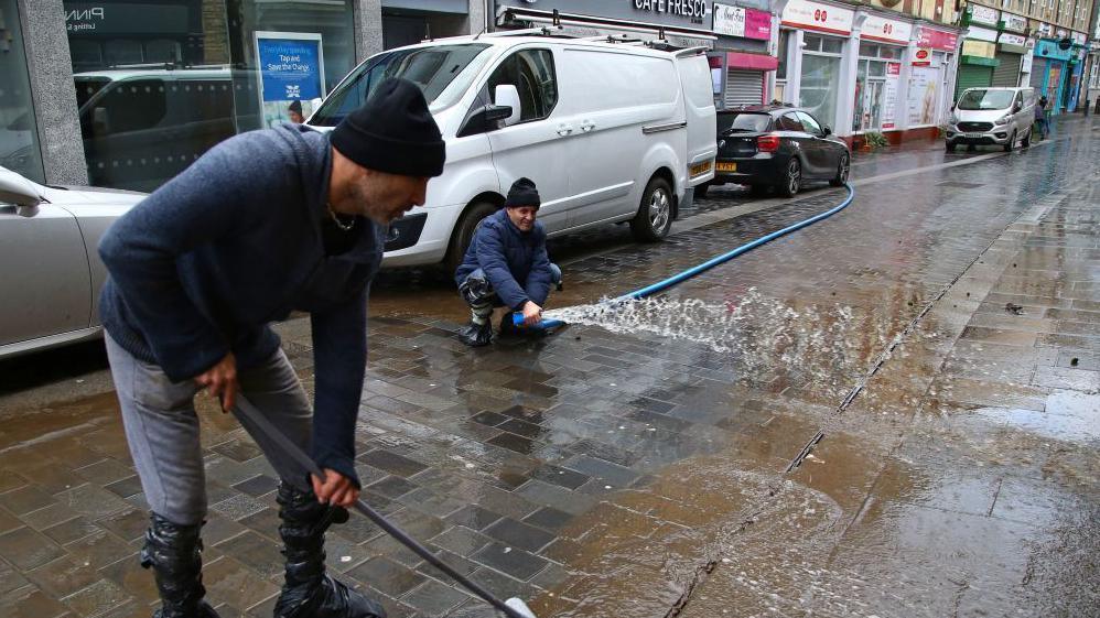 Two men clearing flood water on Mill Street in February 2020