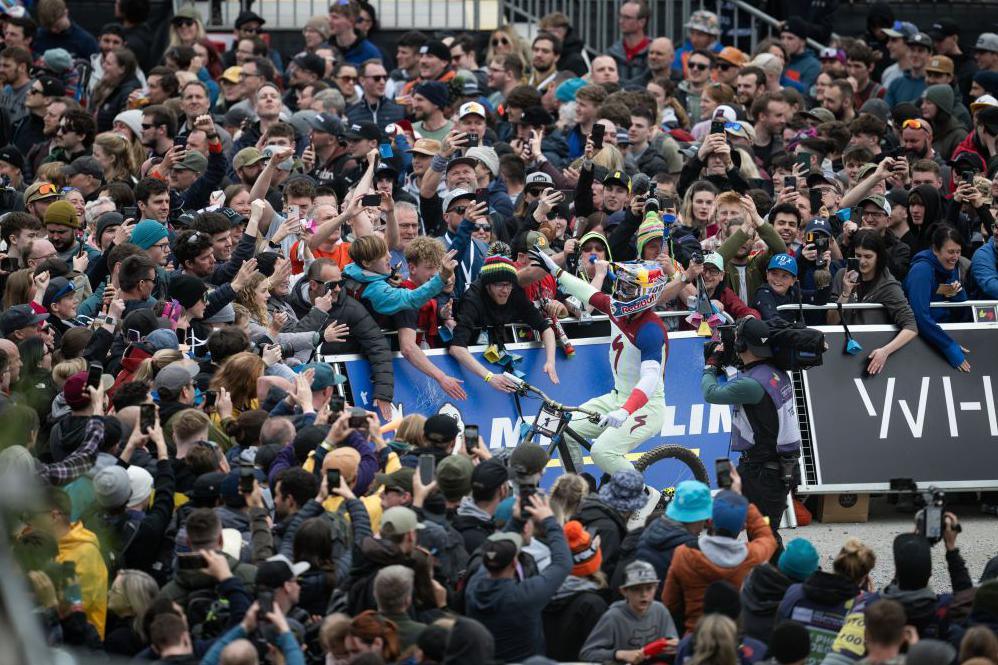 A mountain biker wearing a helmet and white, red and blue clothing celebrates with spectators