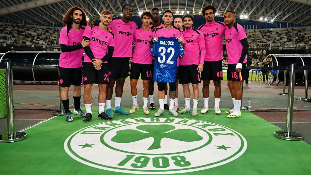 Chelsea players hold up a shirt with 'Baldock 32' on it