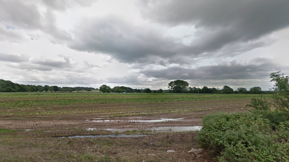 An area of muddy farm land, lined with trees 