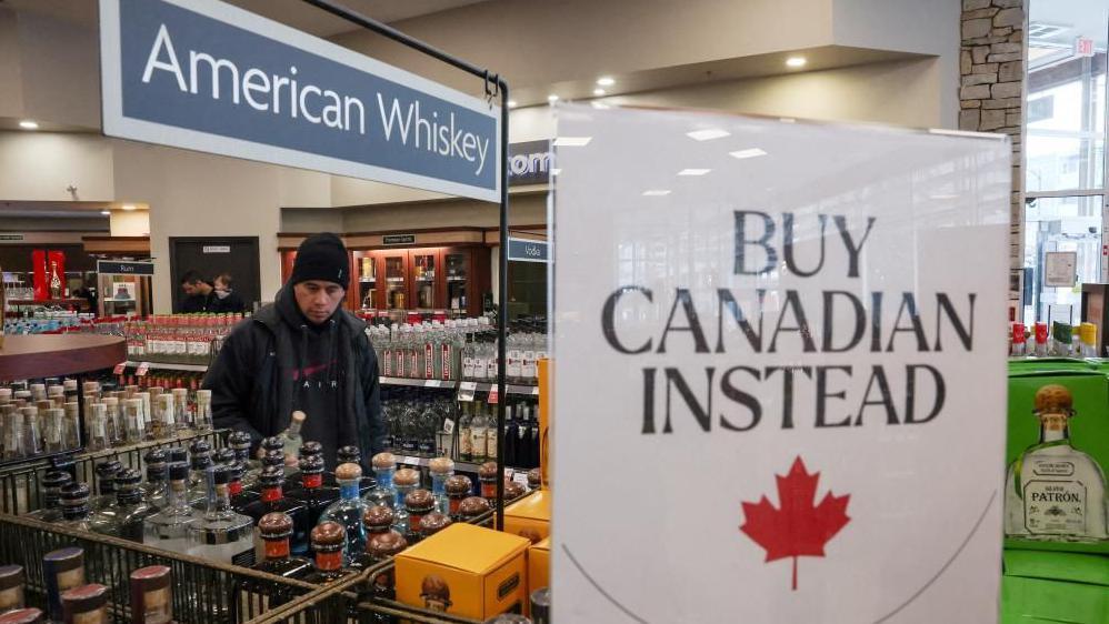 A customer holds a bottle as a sign that reads ''Buy Canadian Instead'' is displayed after the top five U.S. liquor brands were removed from sale at B.C. Liquor Stores, as part of a response to U.S. President Donald Trump's 25% tariffs on Canadian goods, in Vancouver, British Columbia, Canada, February 2, 2025.