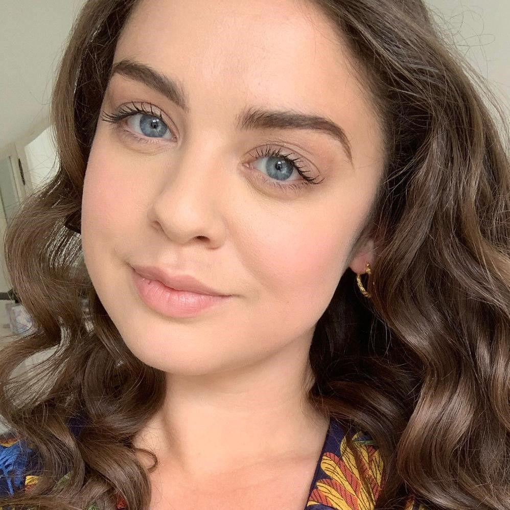Person with long, curly brown hair wearing a dark blue shirt with a colourful floral pattern.