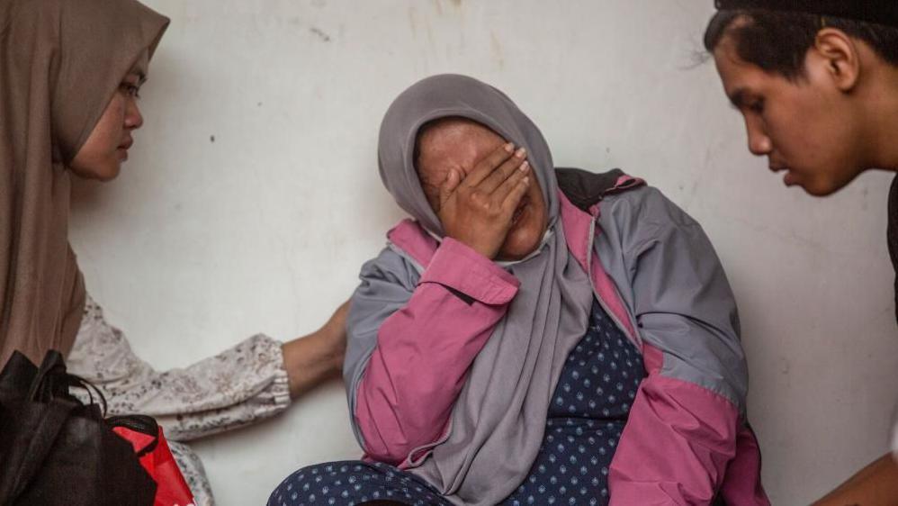 A relative in a pink jacket weeps as a rescue operation is underway at Al Khoziny Islamic Boarding School in East Java, which collapsed while under construction