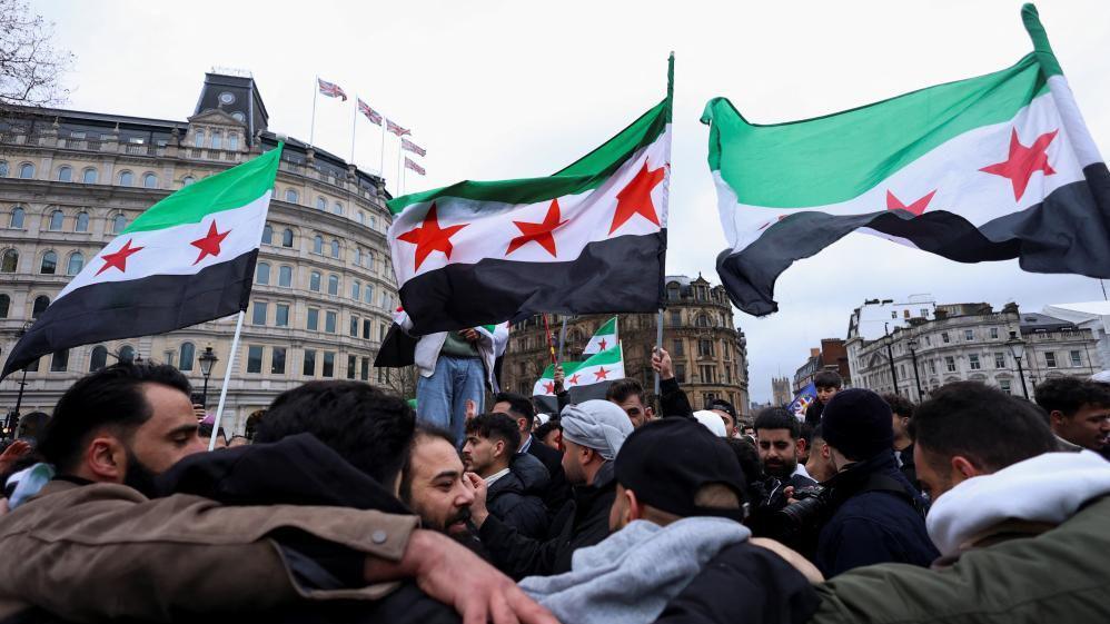 People wave Syrian opposition flags as they gather in Trafalgar Square, in London, on December 8, 2024