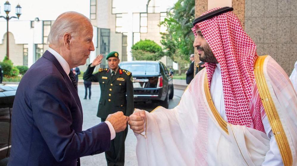Biden përplas grushtin me MBS ndërsa një roje sigurie përshëndet në sfond.