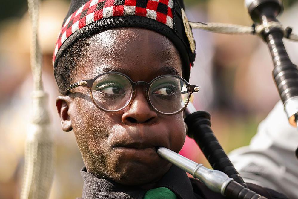 Close-up of a young person in round glasses playing the bagpipes.