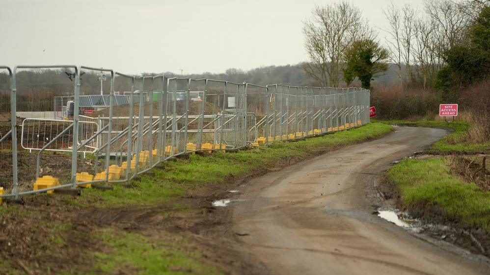 A country road with fields around it that have metal fencing on it. It looks like a construction site. 