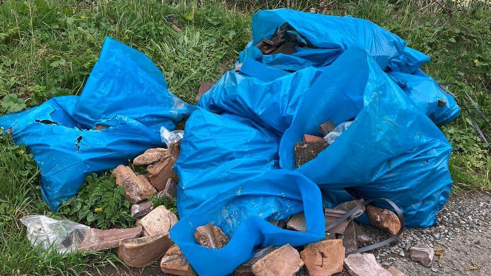 Blue plastic bags full of rubble sitting on grass