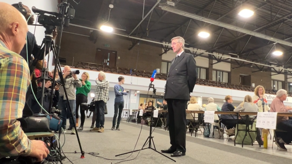 Jacob Rees-Mogg standing in front of a microphone at an election count. 