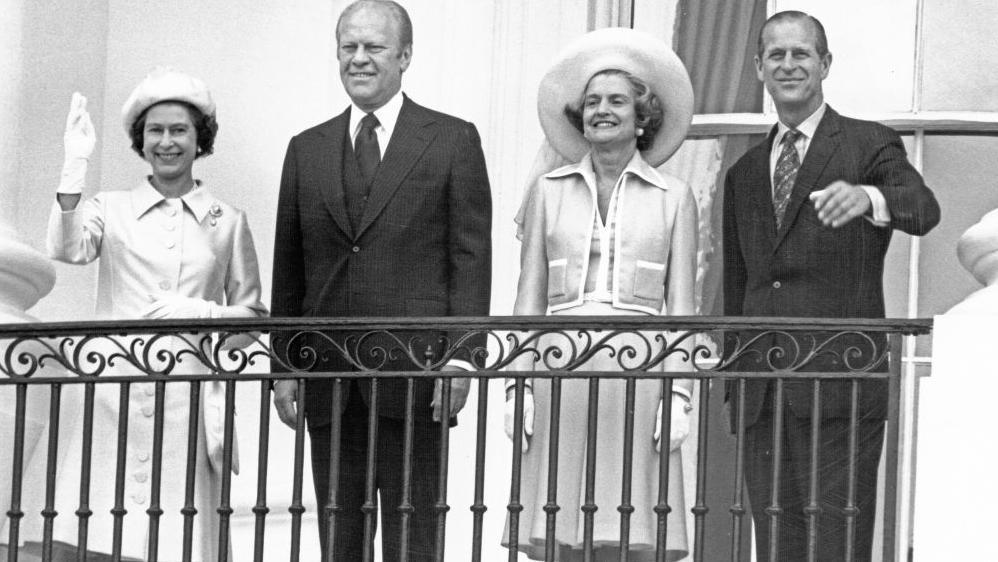 Mbretëresha Elizabeth II, Presidenti i SHBA-së Gerald Ford, Zonja e Parë e SHBA-së Betty Ford dhe Princi Philip, Duka i Edinburgut, përshëndetin shikuesit në këtë imazh bardhë e zi.