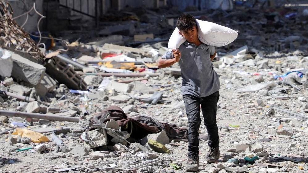 Palestinian boy carries a bag with flour at Sabra neighbourhood, following Israeli operation, in Gaza City, October 8, 2025