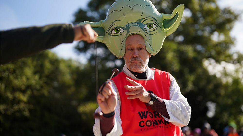 man dressed as yoda from Star Wars, playing conkers.