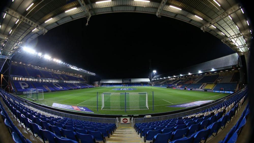 Peterborough United's Weston Homes Stadium: a view from behind a goal showing a green pitch and four stands filled with blue seats.