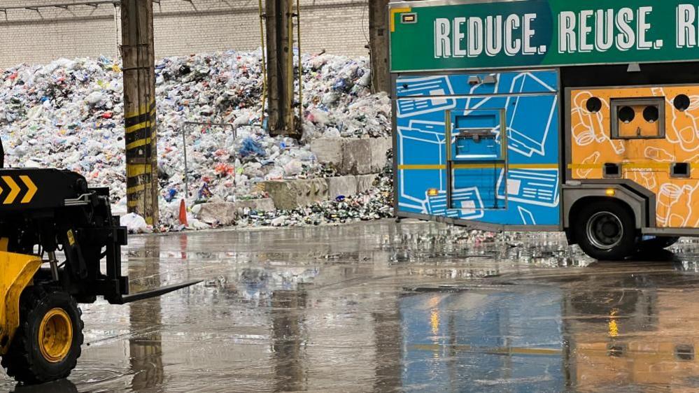 A green, yellow and blue waste collection truck from Swindon Borough Council arrives at the depot ready to unload waste