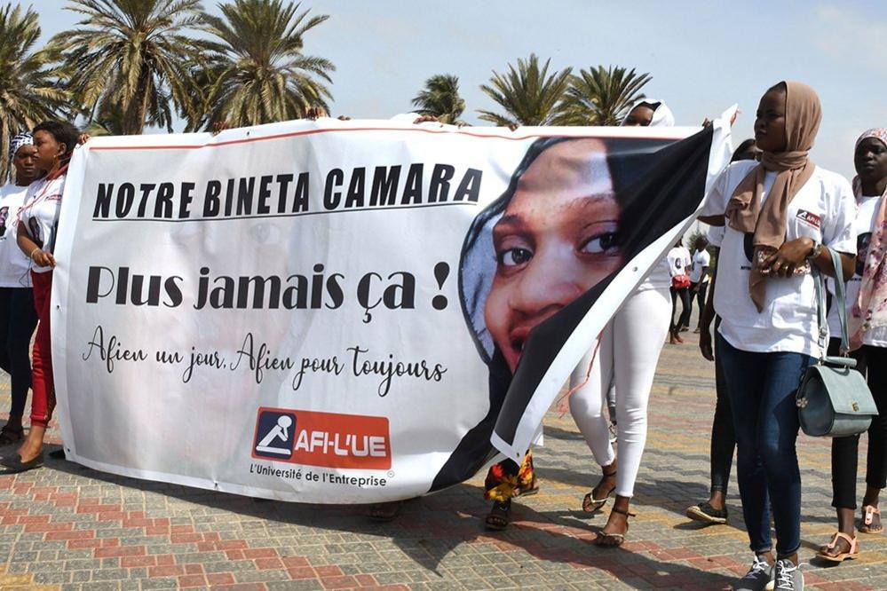 Women hold up a banner with a picture of Bineta Camara and the slogan "Never again" in Dakar in May 2019