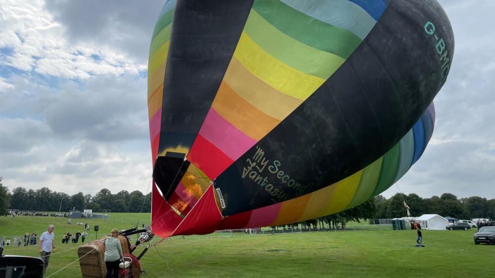 Rainbow-coloured balloon inflates and starts to lift off the ground at the Racecourse.  