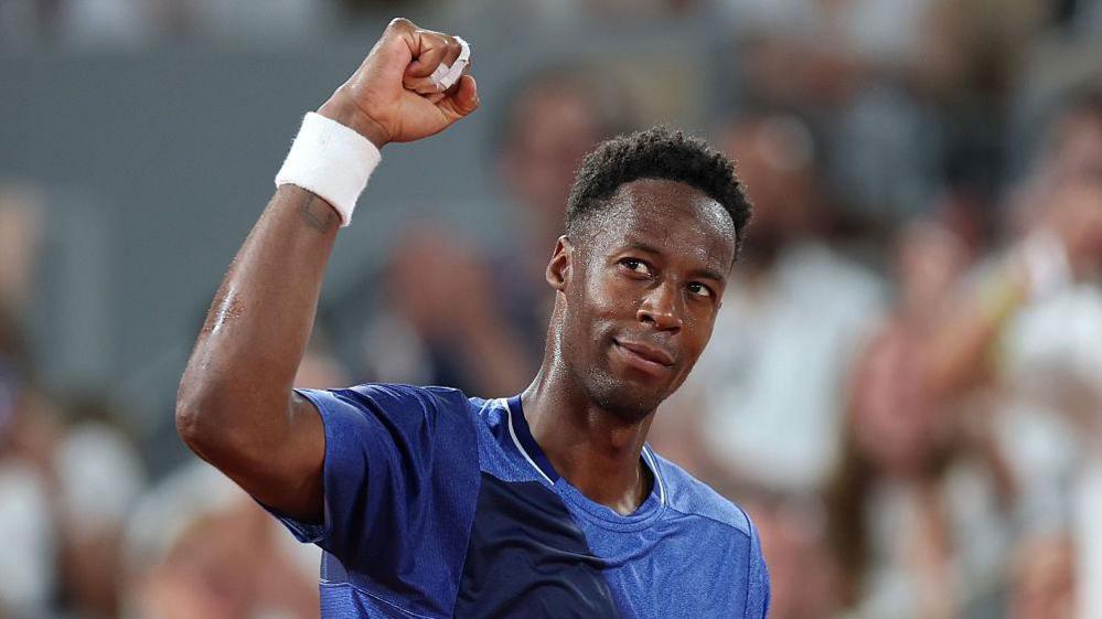 Gael Monfils, wearing a blue t-shirt, looks up to his right and raises his right fist