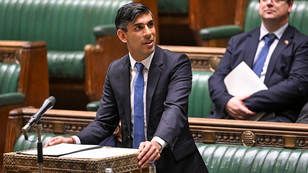 Sunak looking away from camera while wearing a suit and blue tie as he speaks in Parliament on 23 January